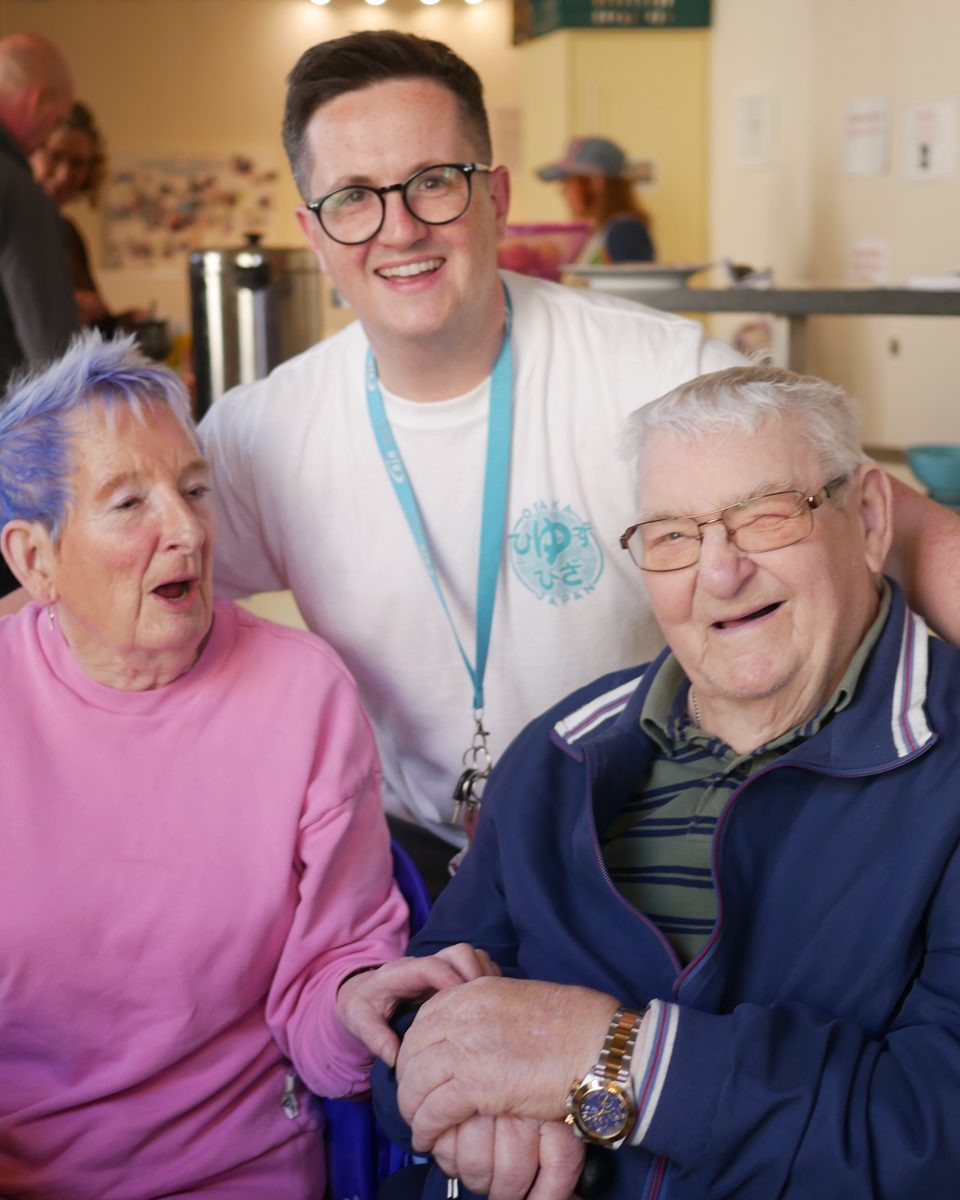 Ryan sharing a laugh with two older people over a cup of tea